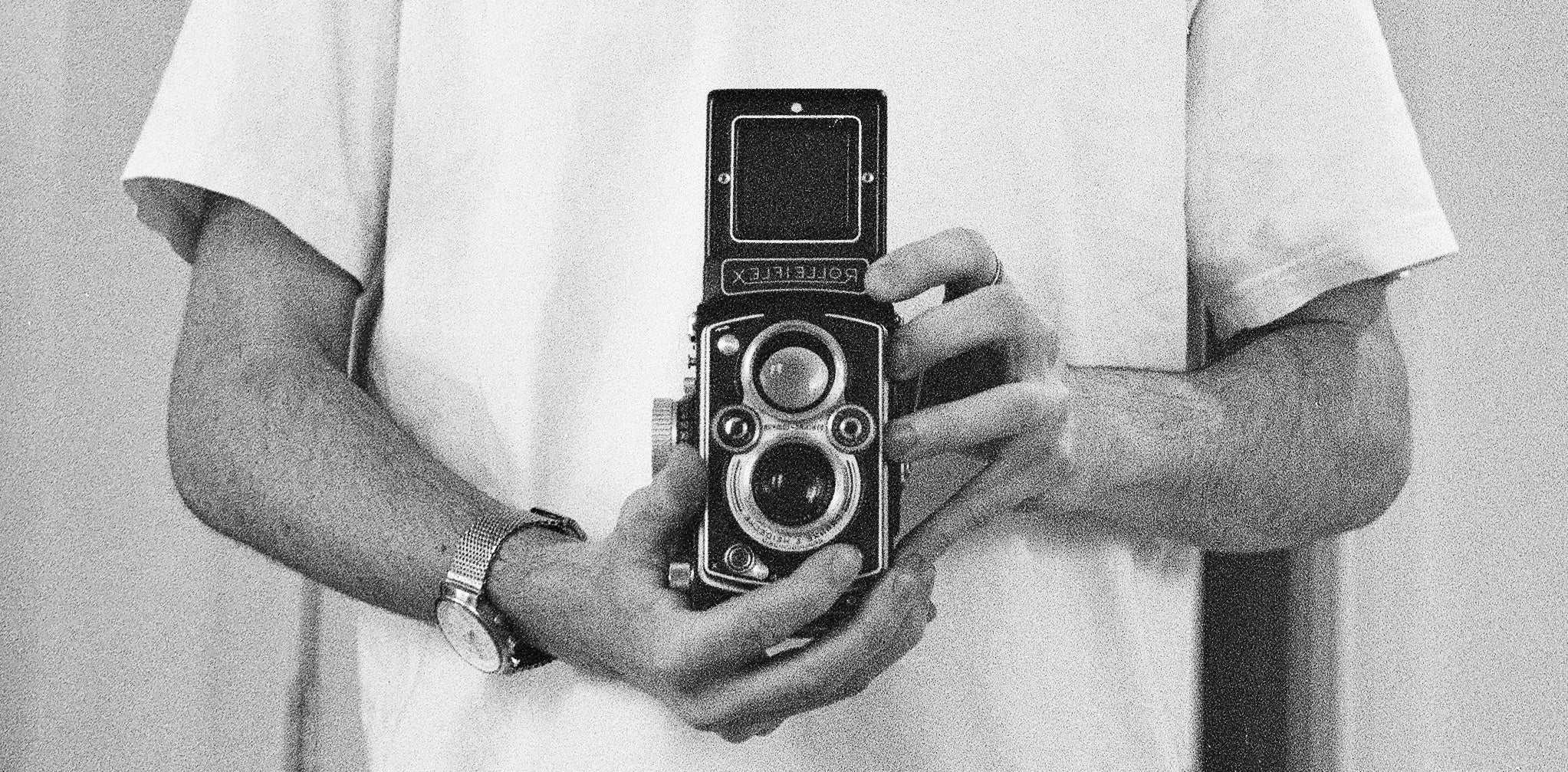 Person holding a vintage camera against a plain background